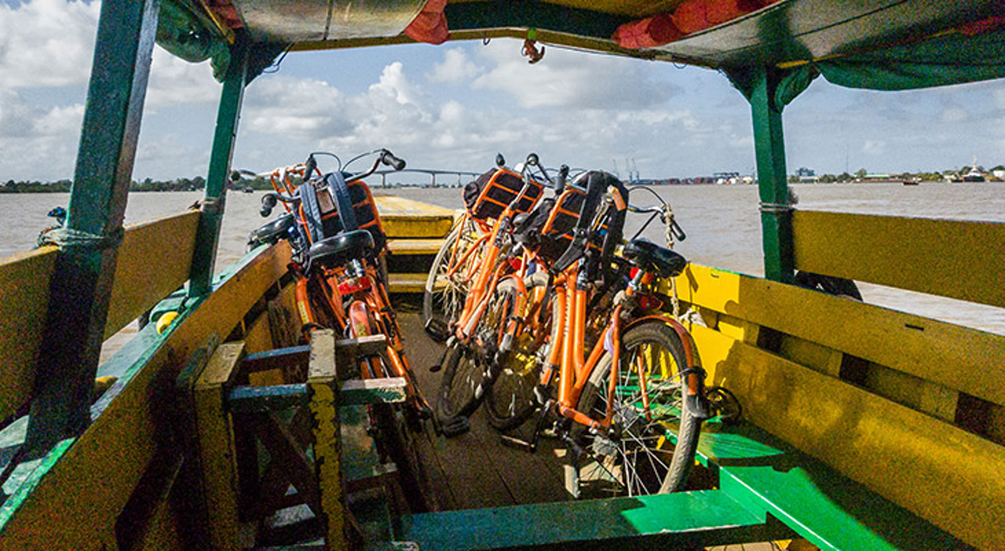 Oranje fietsen op een boot tijdens een overtocht over een brede rivier, met brug op de achtergrond.
