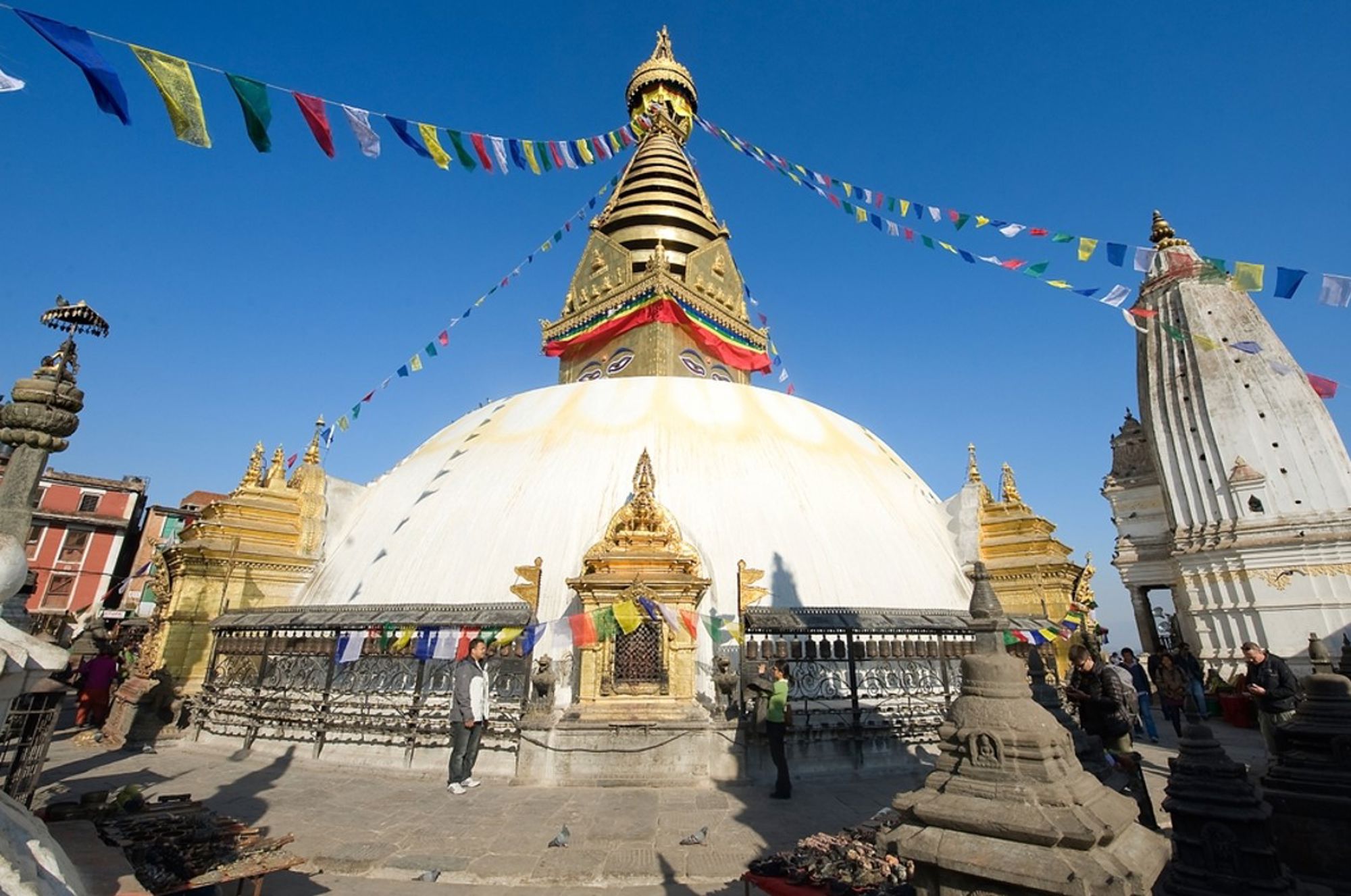 Boudhanath-stoepa in Kathmandu, Nepal, met gebedsvlaggen en gouden toren onder een heldere blauwe lucht.