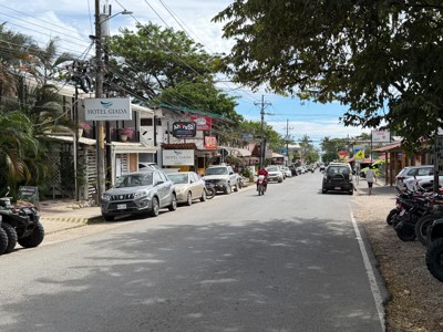 Straatbeeld in Sámara, Costa Rica, met Hotel Giada, geparkeerde auto’s en een motorrijder.