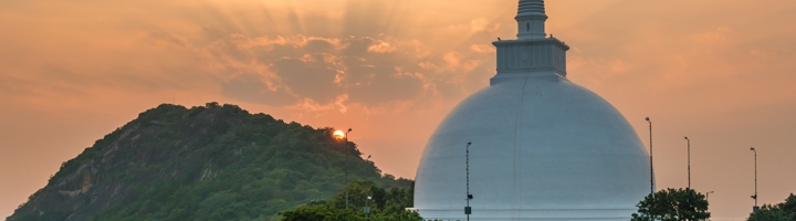 Witte boeddhistische stoepa in Sri Lanka bij zonsondergang, omringd door groene heuvels.