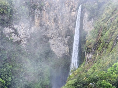 Hoge waterval die langs een steile rotswand in een groene kloof op Sumatra naar beneden stort.