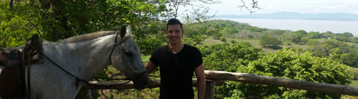 Man poseert met een paard bij een uitkijkpunt met groen landschap en zee op de achtergrond in Costa Rica.
