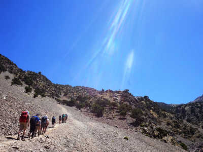 Wandelaars met rugzakken klimmen via een bergpad tijdens de beklimming van Mt. Toubkal in Marokko.