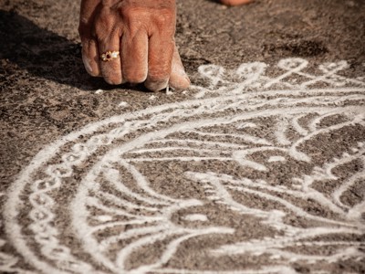 Hand tekent een rangoli-patroon met wit poeder op straat tijdens de Route Zuid-India.