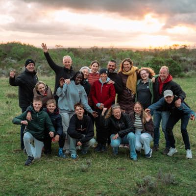 Gezin met gids op safari in Tanzania, met verrekijkers en camera’s in de wildernis.