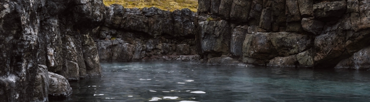 Geothermisch bad tussen lavastenen in IJsland, met damp boven het water.