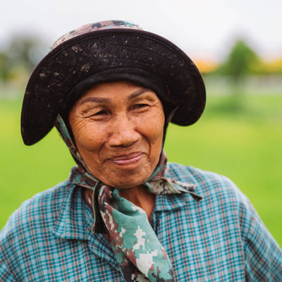 Portret van een Thaise vrouw met hoed en sjaal in een groen rijstveld tijdens familiereis Thailand Noord en Zuid.