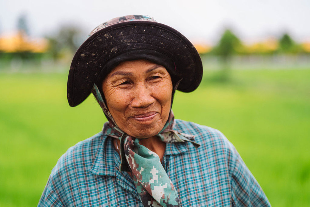 Portret van een Thaise vrouw met hoed en sjaal in een groen rijstveld tijdens familiereis Thailand Noord en Zuid.