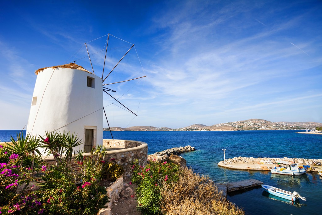 Witte windmolen aan zee op Naxos, met kleine haven en bootjes in de Cycladen, Griekenland.