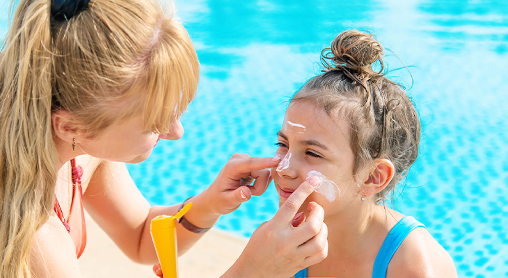 Zonnebrand voor kinderen Moeder smeert zonnebrandcrème op het gezicht van haar dochter bij het zwembad.