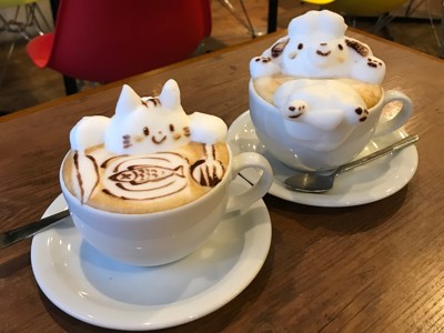 Latte art in een Japans café: cappuccino’s met schuimfiguren van een kat en een hond op tafel.