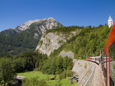 Treinreis door berglandschap in Centraal Europa, langs groene valleien en rotswanden onder een blauwe lucht.