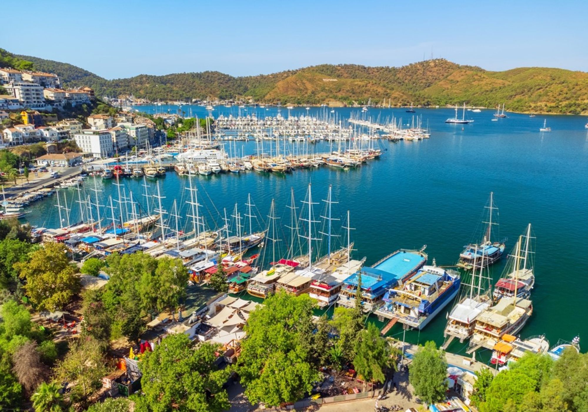 Jachthaven met zeilboten in een baai aan de Turkse kust, omringd door heuvels en stadje.