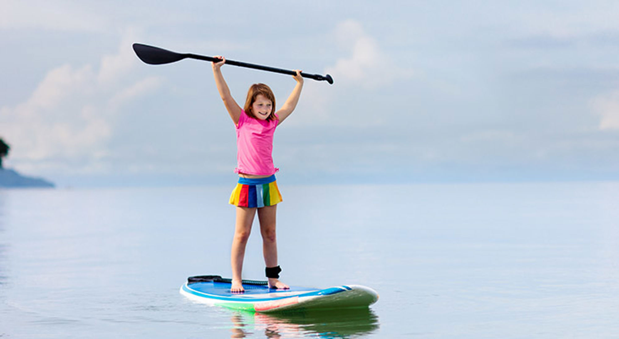 Meisje op een SUP-board op rustig water houdt een peddel boven haar hoofd.
