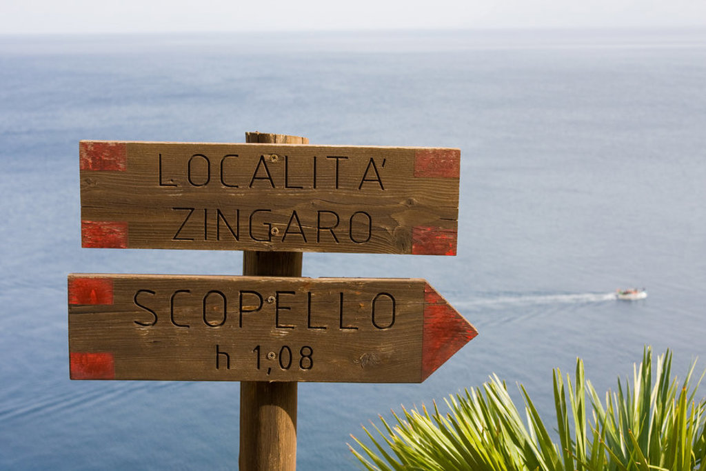 Wandelroutebord naar Zingaro en Scopello aan de kust van West-Sicilië, met zee op de achtergrond.
