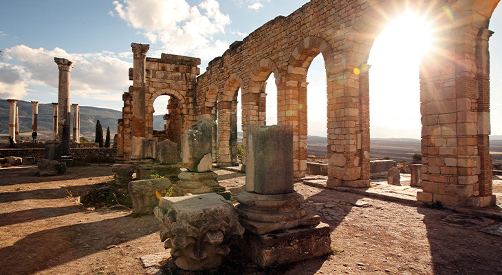 Volubilis Marokko Romeinse ruïnes met bogen en zuilen in tegenlicht, met uitzicht over het landschap.