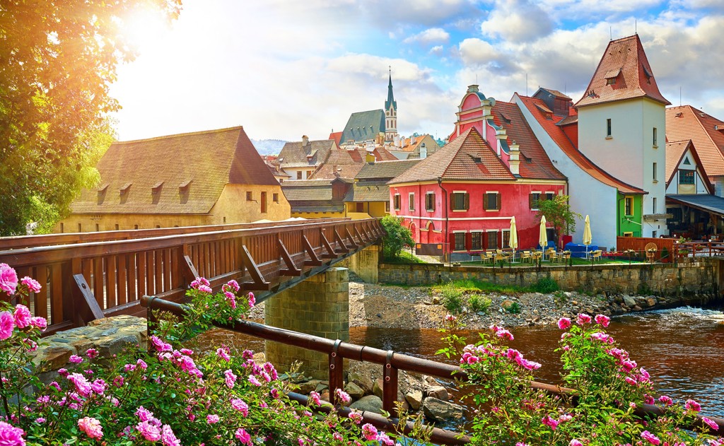 Historische binnenstad in Centraal Europa met houten brug, rivier en kleurrijke huizen.