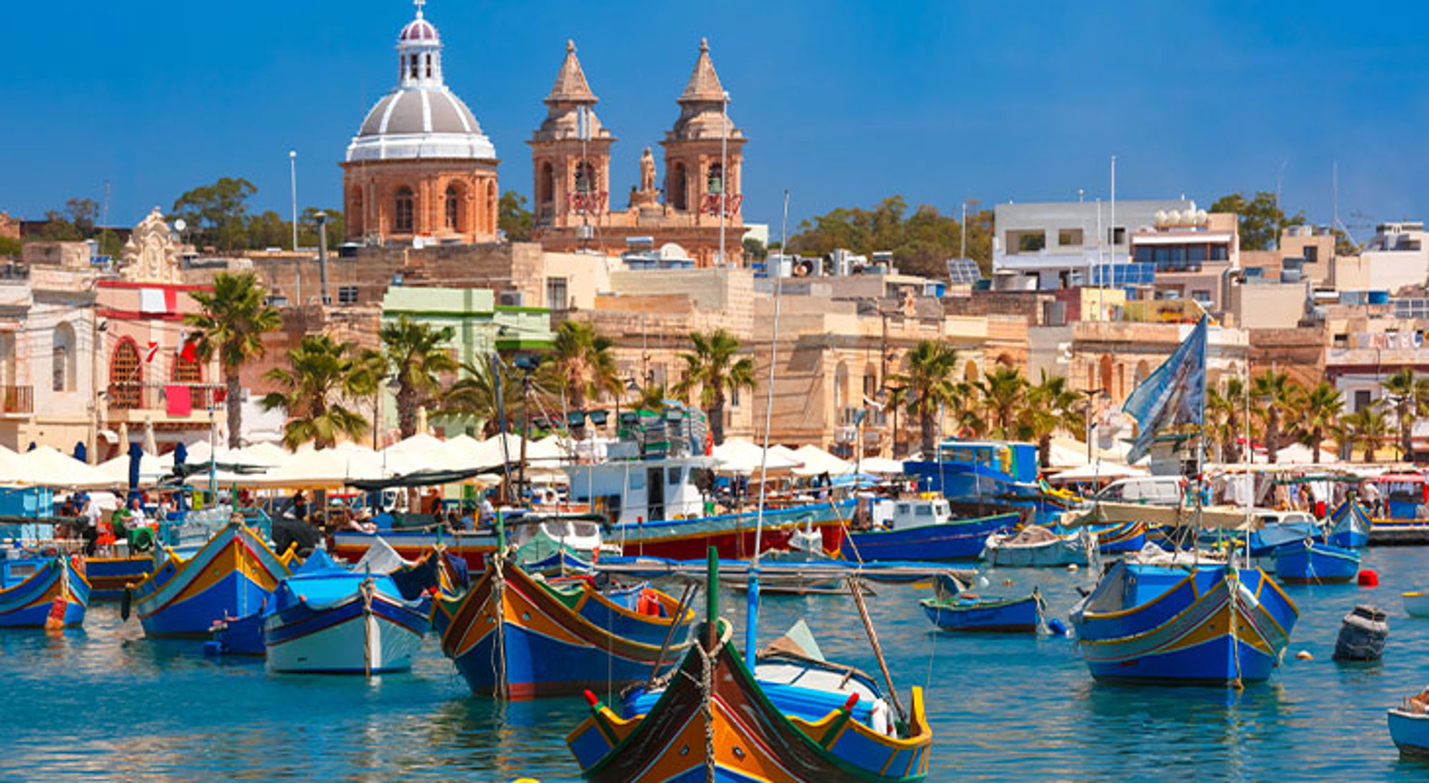 Malta Kleurrijke vissersboten in de haven met de skyline en kerkkoepel op de achtergrond.