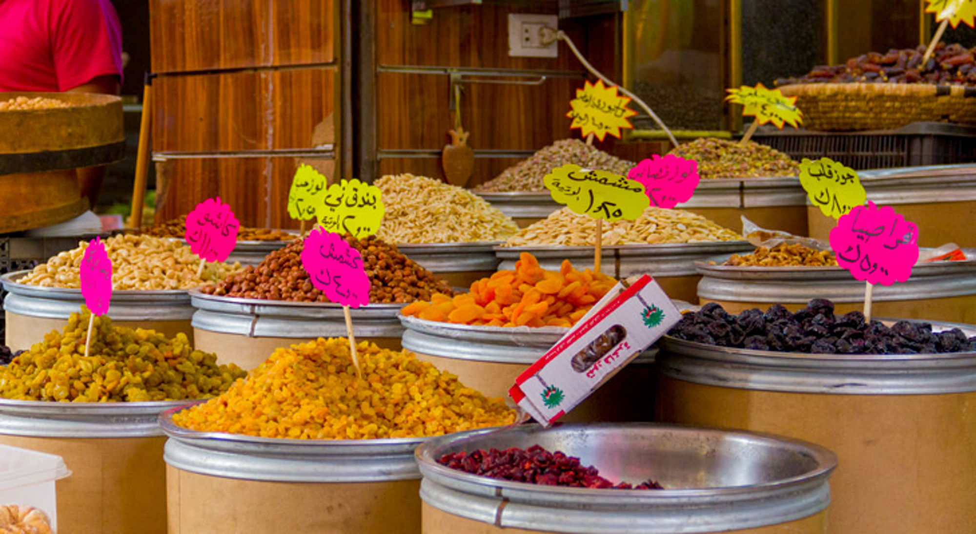 Kramen met gedroogd fruit en noten op een markt, met kleurrijke prijskaartjes in Arabisch schrift.