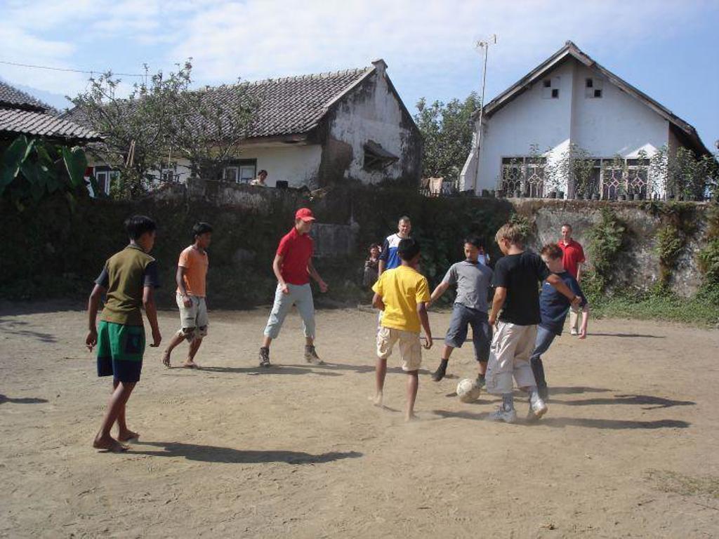 Kinderen en volwassenen spelen voetbal op een zandveld in een dorp op Java tijdens de familiereis Java & Bali.