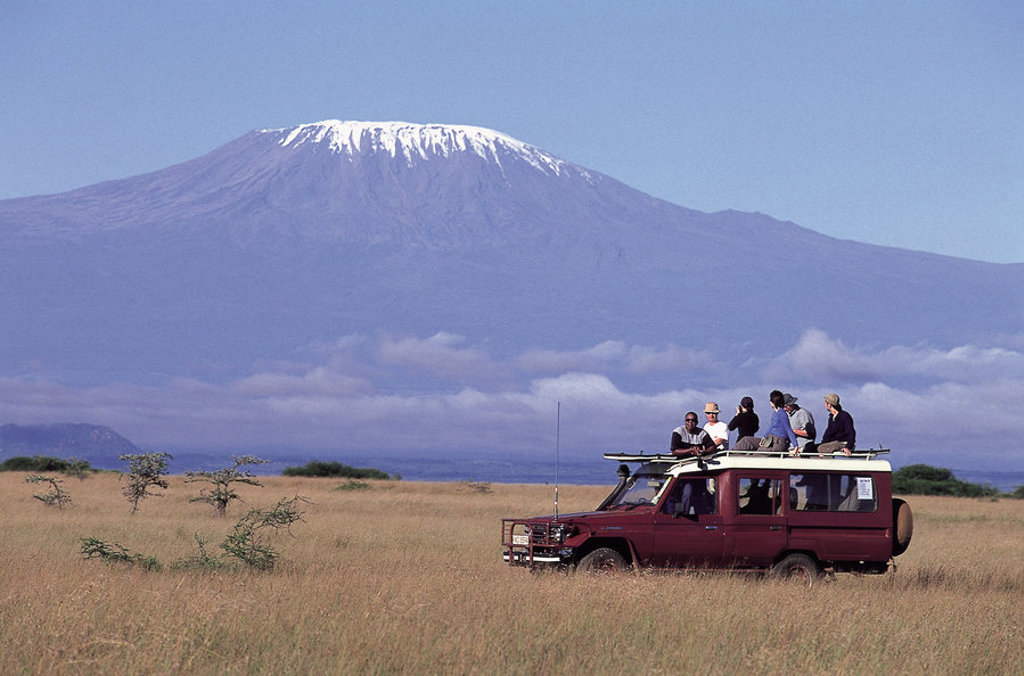 Safari-jeep met reizigers op de savanne, met de besneeuwde Kilimanjaro op de achtergrond in Kenia en Tanzania.