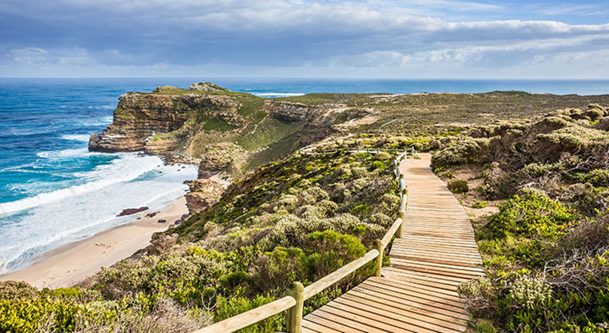 Uitzicht bij Kaap de Goede Hoop Houten wandelpad langs ruige kustkliffen en strand in Zuid-Afrika, met uitzicht op de oceaan.