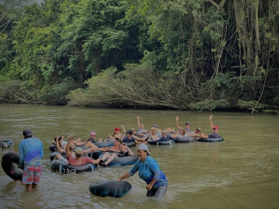 Familiegroep tubet over een rivier in Colombia, begeleid door gidsen langs dichtbegroeide jungle-oevers.