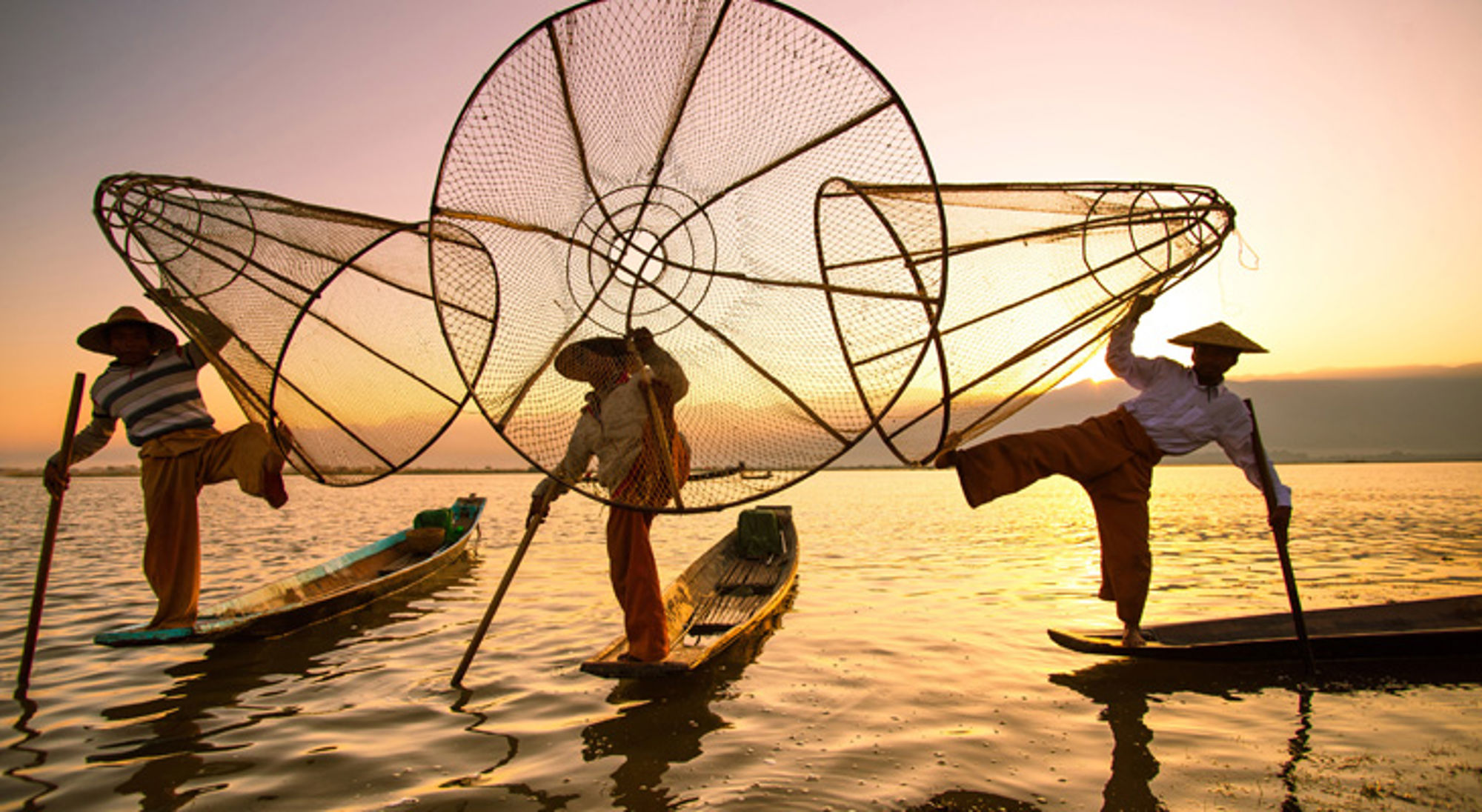 Vissers in Myanmar Vissers met grote netten op traditionele boten bij zonsondergang op het water.