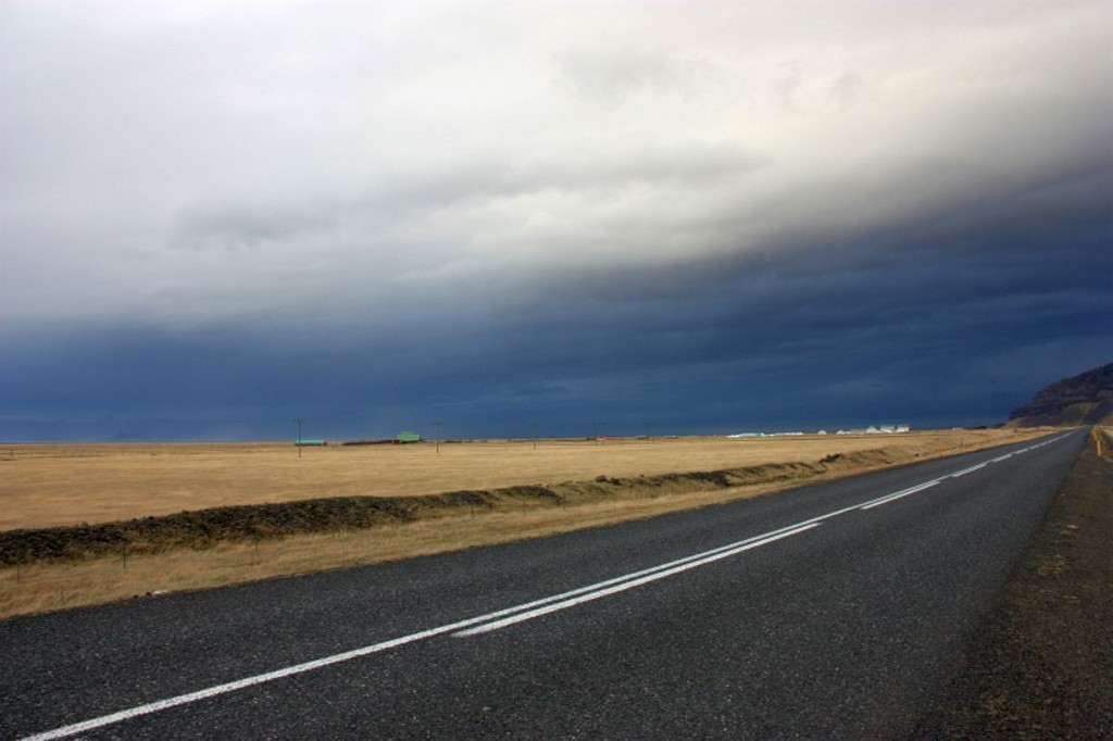 Lange, lege weg door het ruige landschap van IJsland onder een dreigende wolkenlucht.