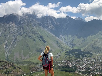 Wandelaar met rugzak kijkt uit over Kazbegi en de Kaukasusbergen in Georgië.