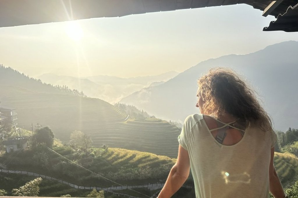 Reiziger kijkt uit over rijstterrassen en bergen in China tijdens groepsrondreis, bij zonsopkomst.