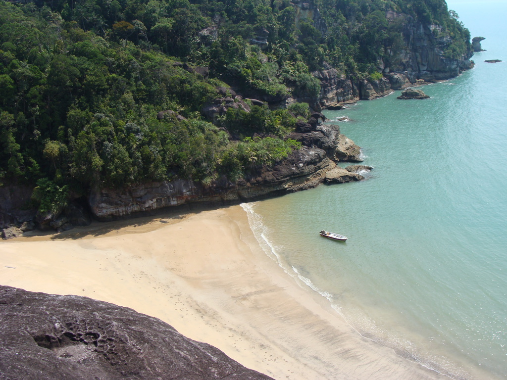 Tropisch strand met rotskliffen en bootje langs de kust van Maleisisch Borneo, Maleisië.