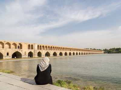 Zittende vrouw aan de rivier met uitzicht op de Si-o-seh Pol-brug in Isfahan, Iran.