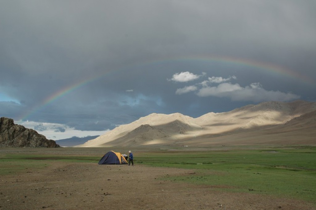 Tent in de Mongoolse steppe met bergen op de achtergrond en een regenboog boven het landschap.