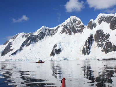 Kajakkers op kalme zee voor besneeuwde bergen en gletsjers in Antarctica tijdens de rondreisroute.