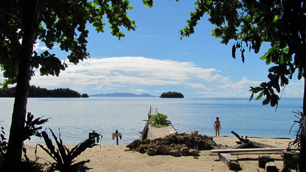 Strand op Sulawesi met houten steiger en uitzicht op rustige zee en eilandjes.
