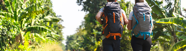 Twee backpackers wandelen langs een spoorlijn door tropisch groen tijdens een wandelvakantie.