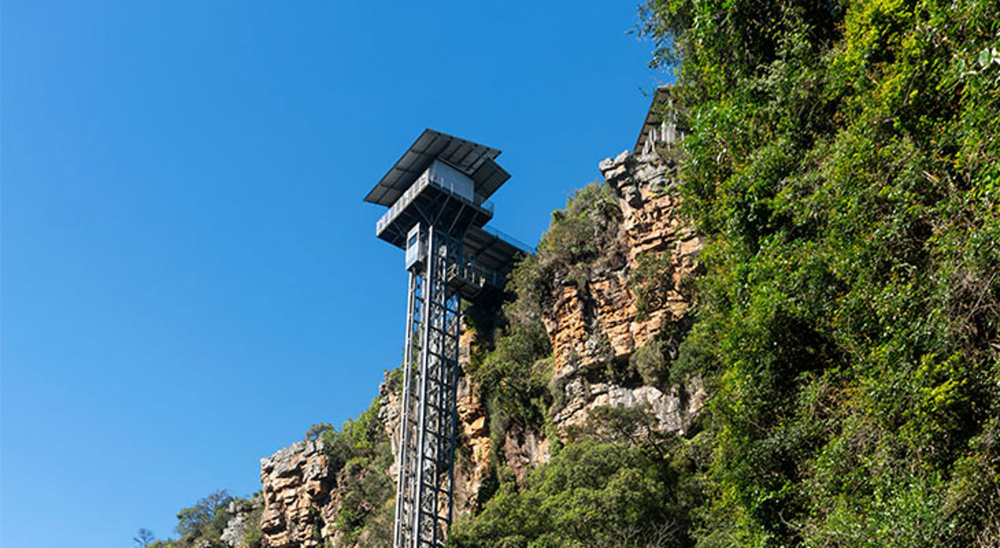Graskop Gorge Lift bij Graskop Uitzichtplatform en lift bij de Tsitsikamma-kloof in Zuid-Afrika, met rotswand en groen tegen een blauwe lucht.
