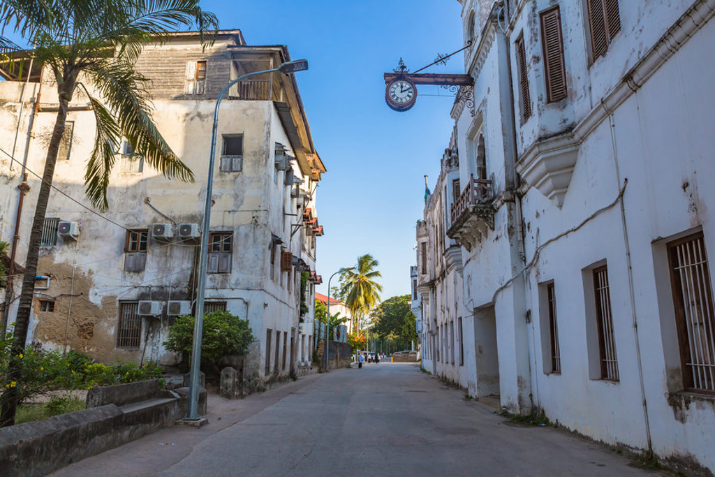 Straat in Stone Town, Zanzibar met witte historische gebouwen, palmbomen en een hangende klok.