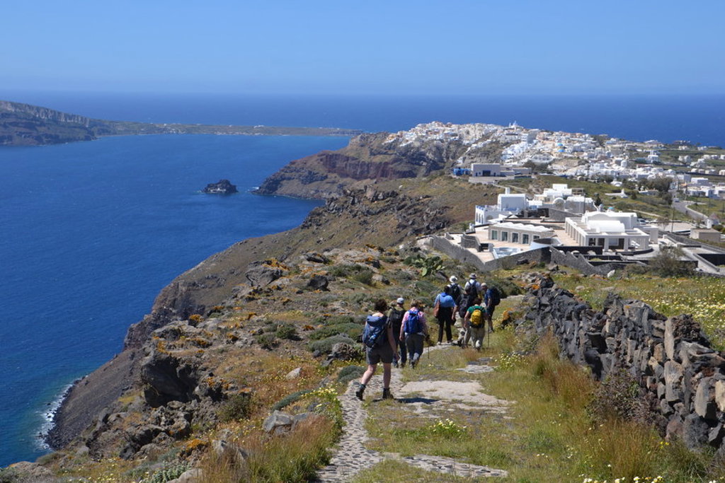Wandelaars op kustpad met uitzicht op de caldera en witte huizen op Santorini, tijdens wandelvakantie Griekenland.
