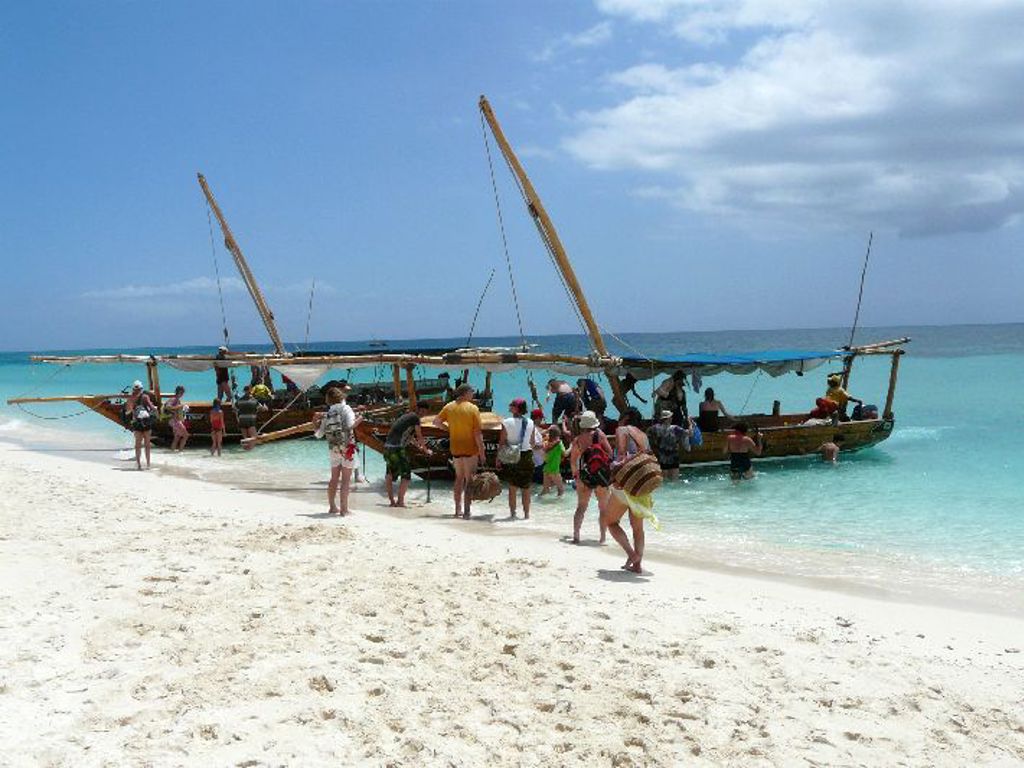 Dhow-boten aan het strand van Zanzibar met reizigers die aan boord gaan tijdens een groepsrondreis Kenia, Tanzania en Zanzibar.