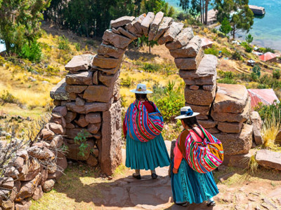 Vrouwen in traditionele kleding lopen door een stenen boog bij het Titicacameer in Peru.
