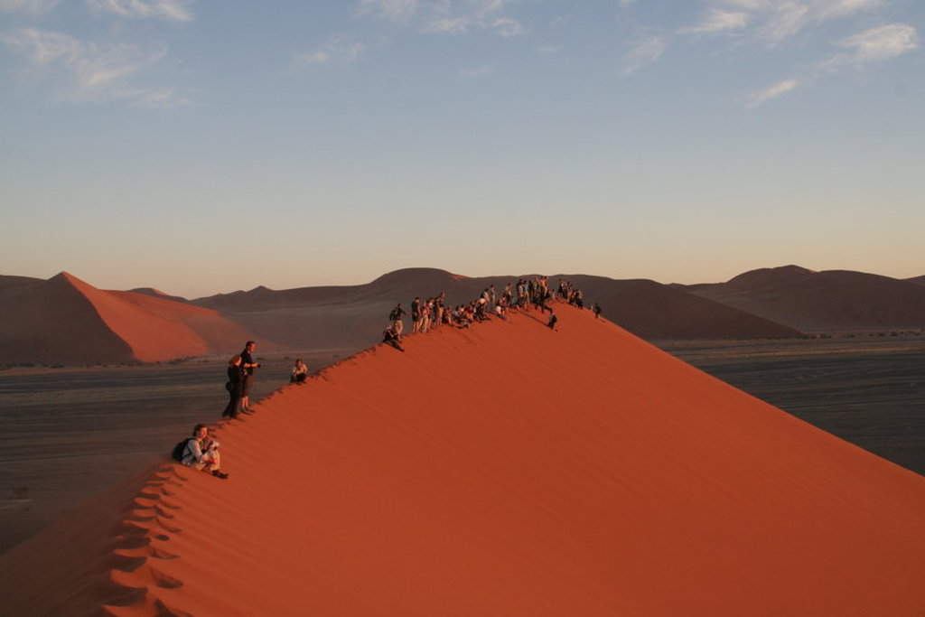Reizigers op een rode zandduin in de Namib-woestijn tijdens een groepsrondreis Namibië.