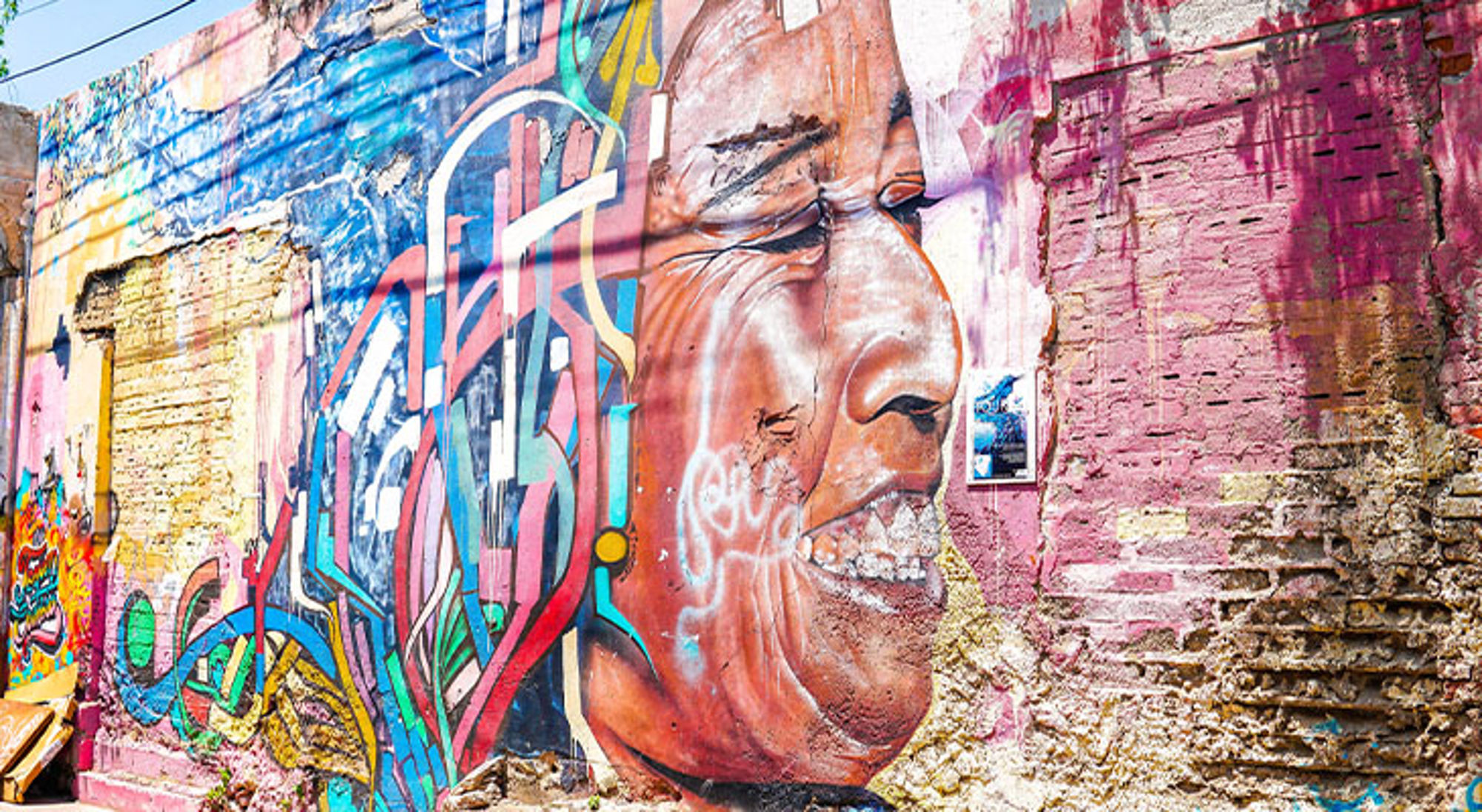 Street art Bogota Kleurrijke muurschildering met een groot gezicht en abstracte graffiti op een verweerde bakstenen muur.