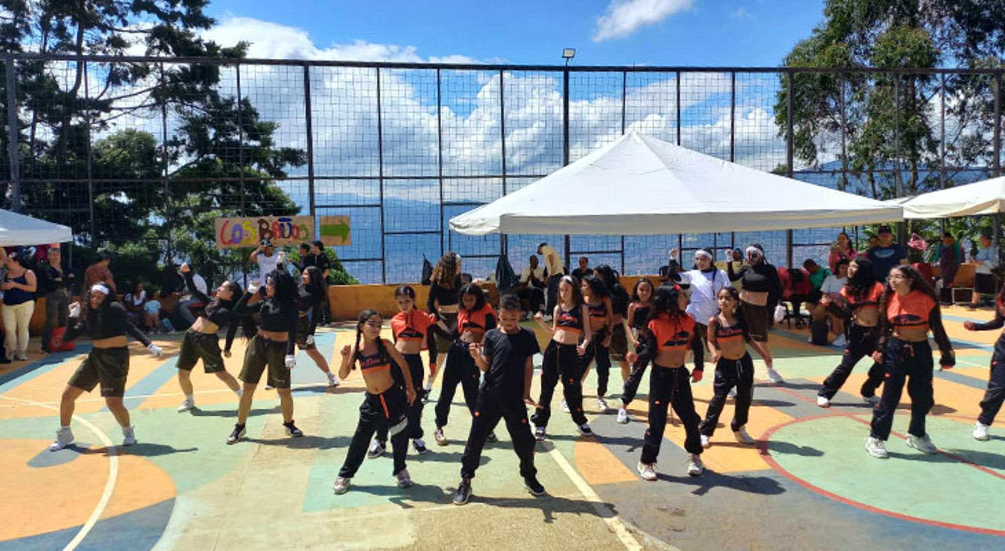 Dans Stichting Children of Medellín Dansgroep voert een choreografie uit op een buitenbasketbalveld tijdens een evenement.