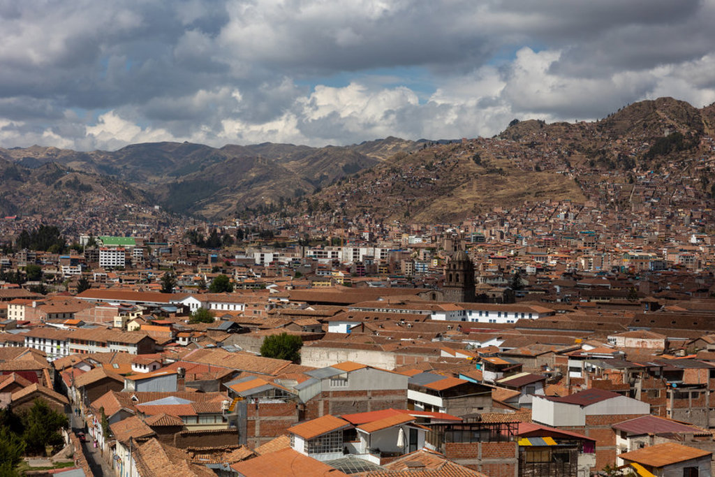 Uitzicht over Cusco met roodbruine daken en Andesbergen onder een bewolkte lucht, tijdens een 22-35ers reis Peru.