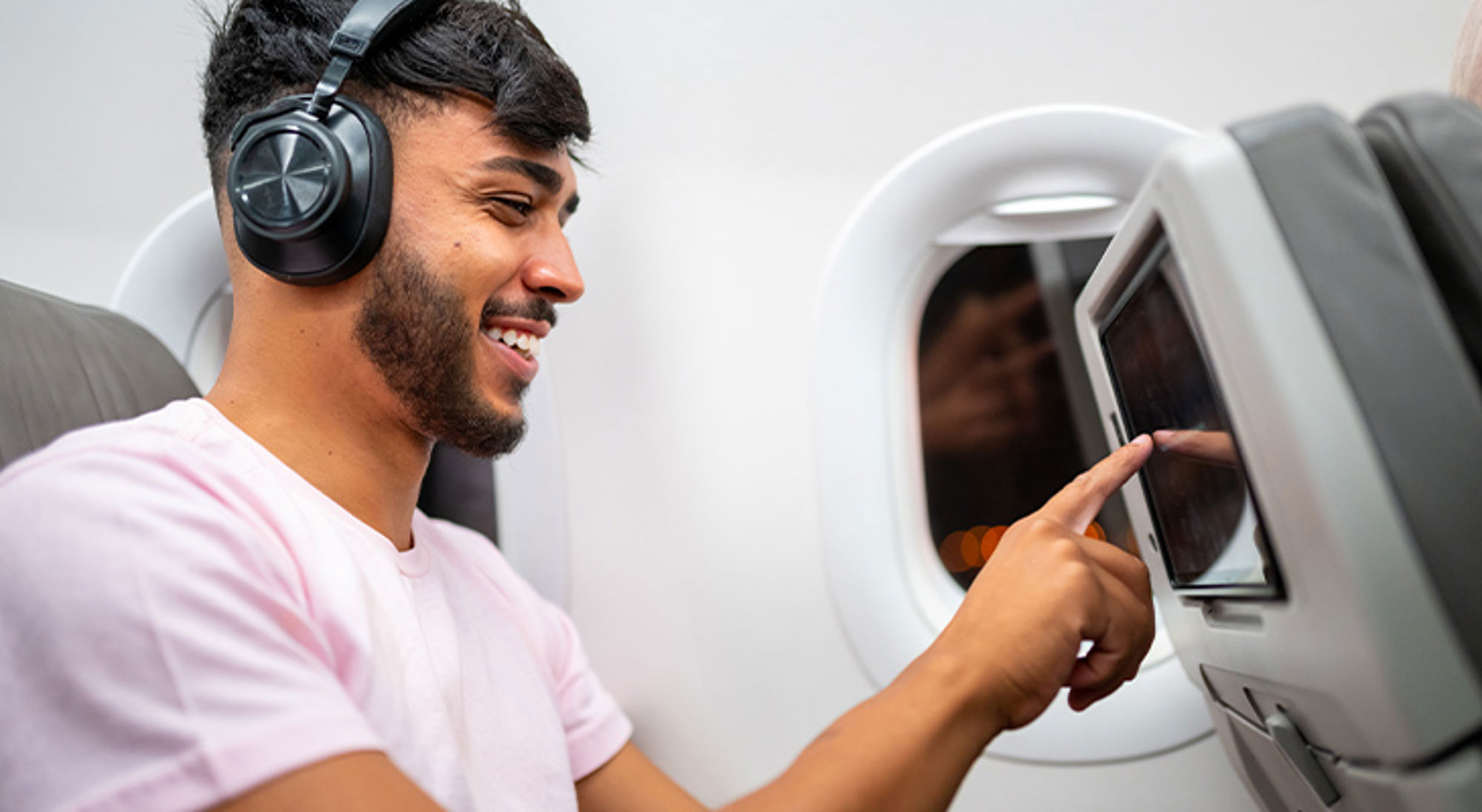 Films kijken in het vliegtuig Passagier met koptelefoon bedient het entertainmentscherm in het vliegtuig.