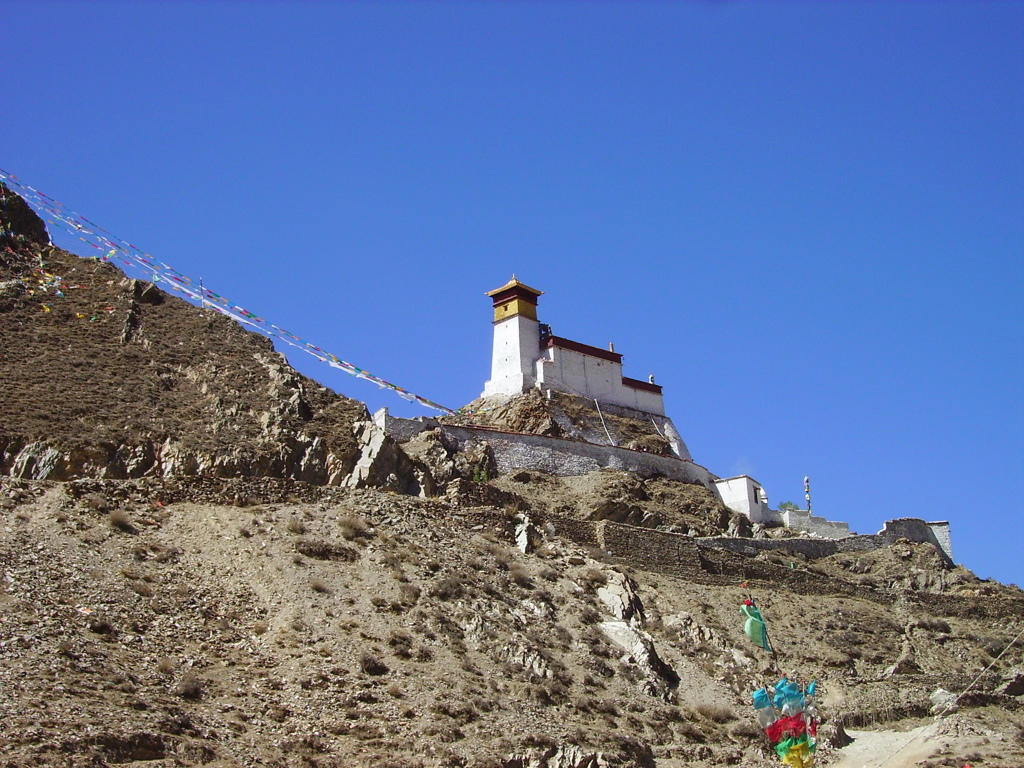 Tibetaans klooster op een rotsachtige heuvel met gebedsvlaggen, tijdens groepsrondreis Tibet en Nepal.