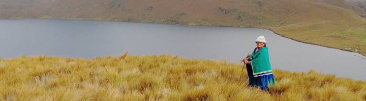Vrouw in traditionele kleding bij een bergmeer in de Andes tijdens een rondreis door Ecuador.
