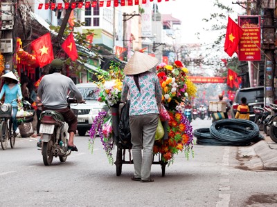 Straatbeeld in Hanoi met bloemenverkoper en Vietnamese vlaggen langs de weg.